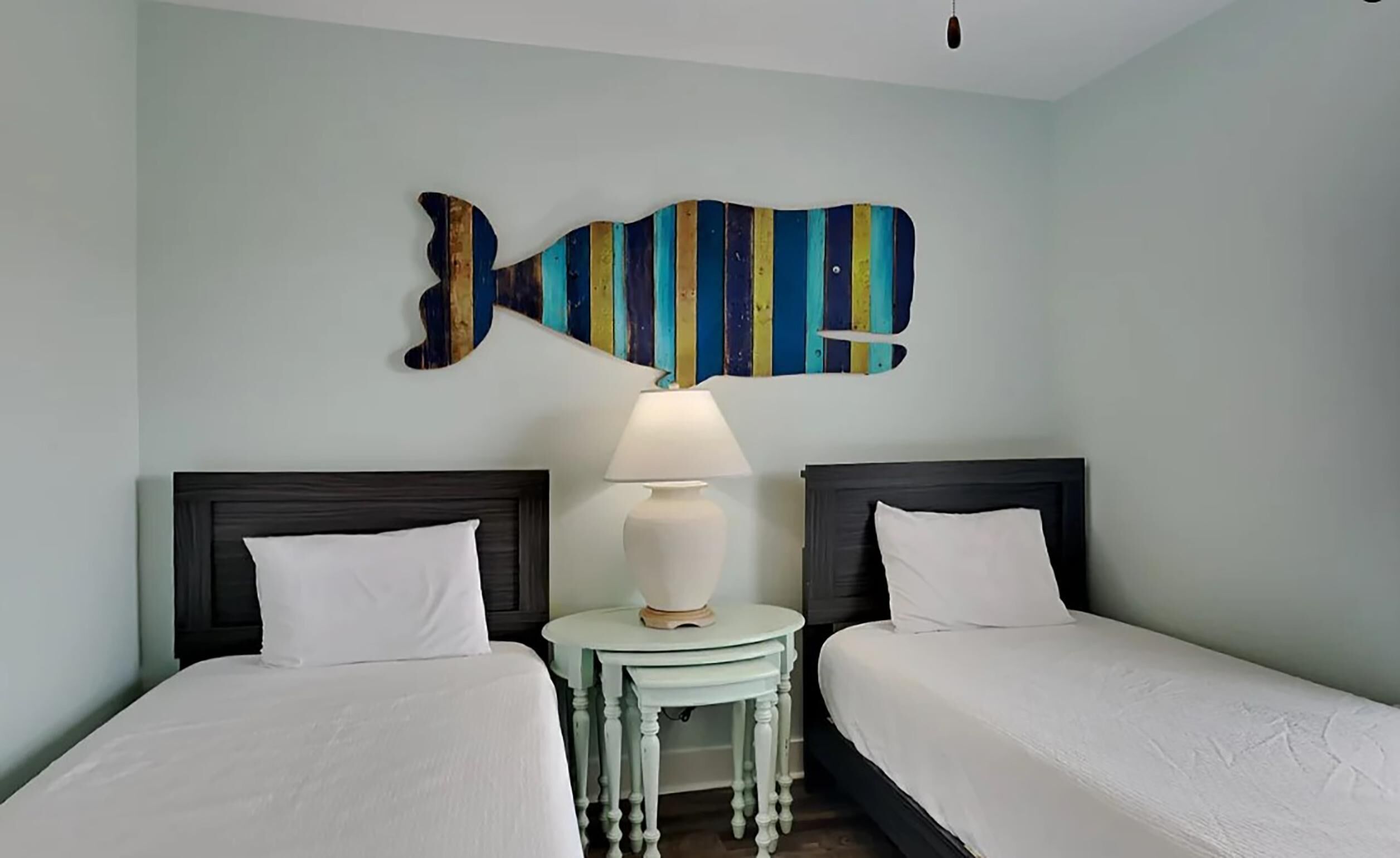 A hotel room with two beds, a small table with a lamp, and a colorful fish-shaped wall decoration.