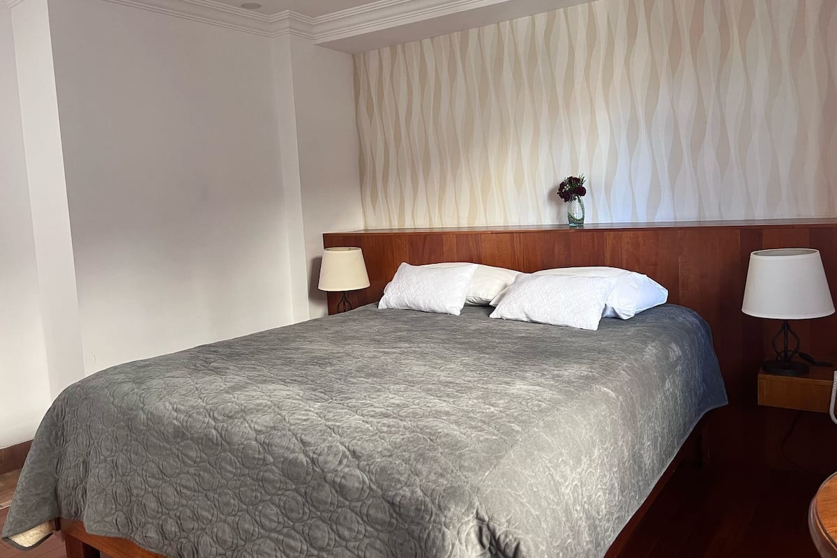 Habitación de hotel con una cama grande, dos lámparas de noche, un cabecero de madera y una pared con estampado.