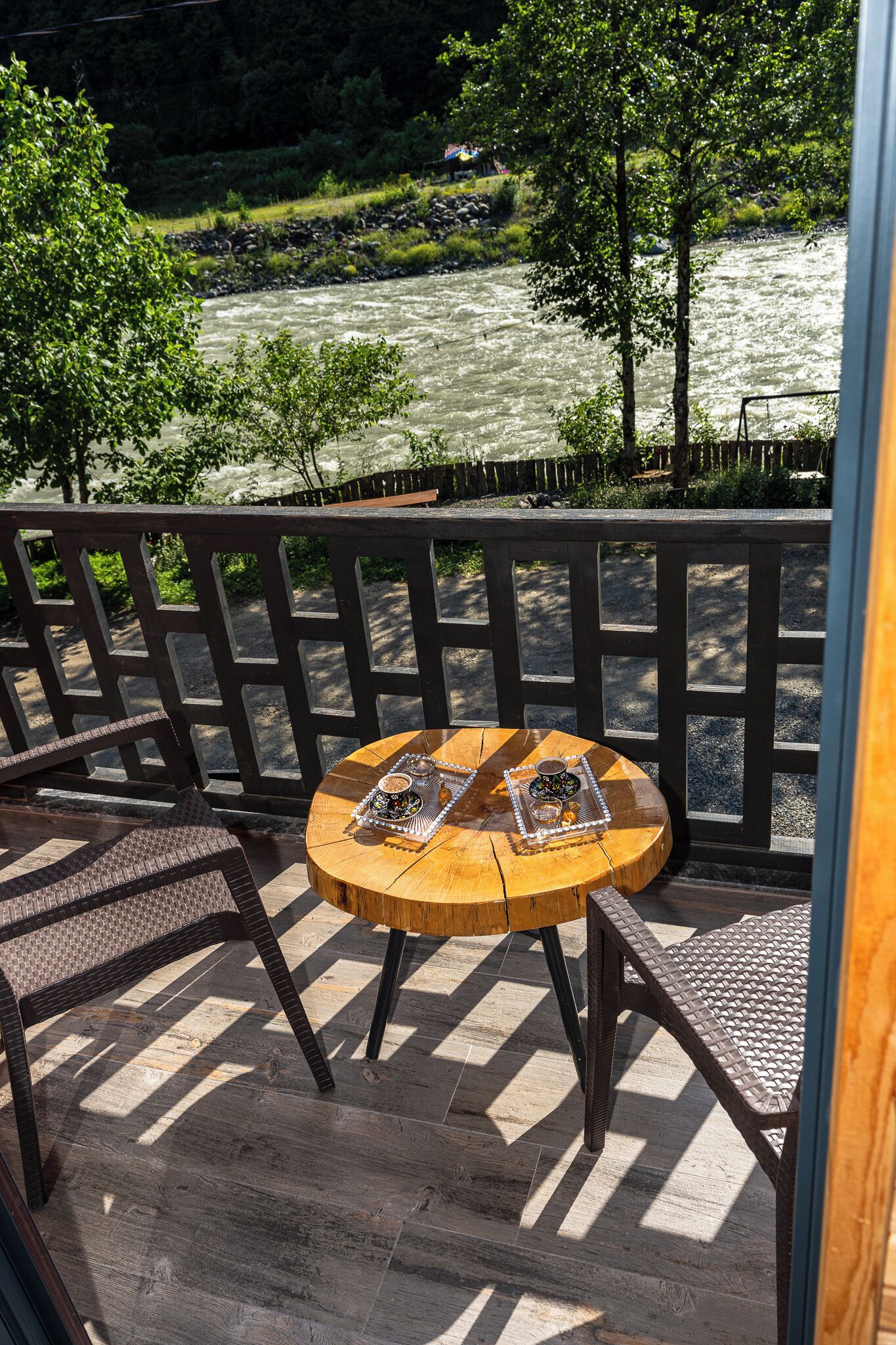 A wooden deck with a round table and chairs, overlooking a river.