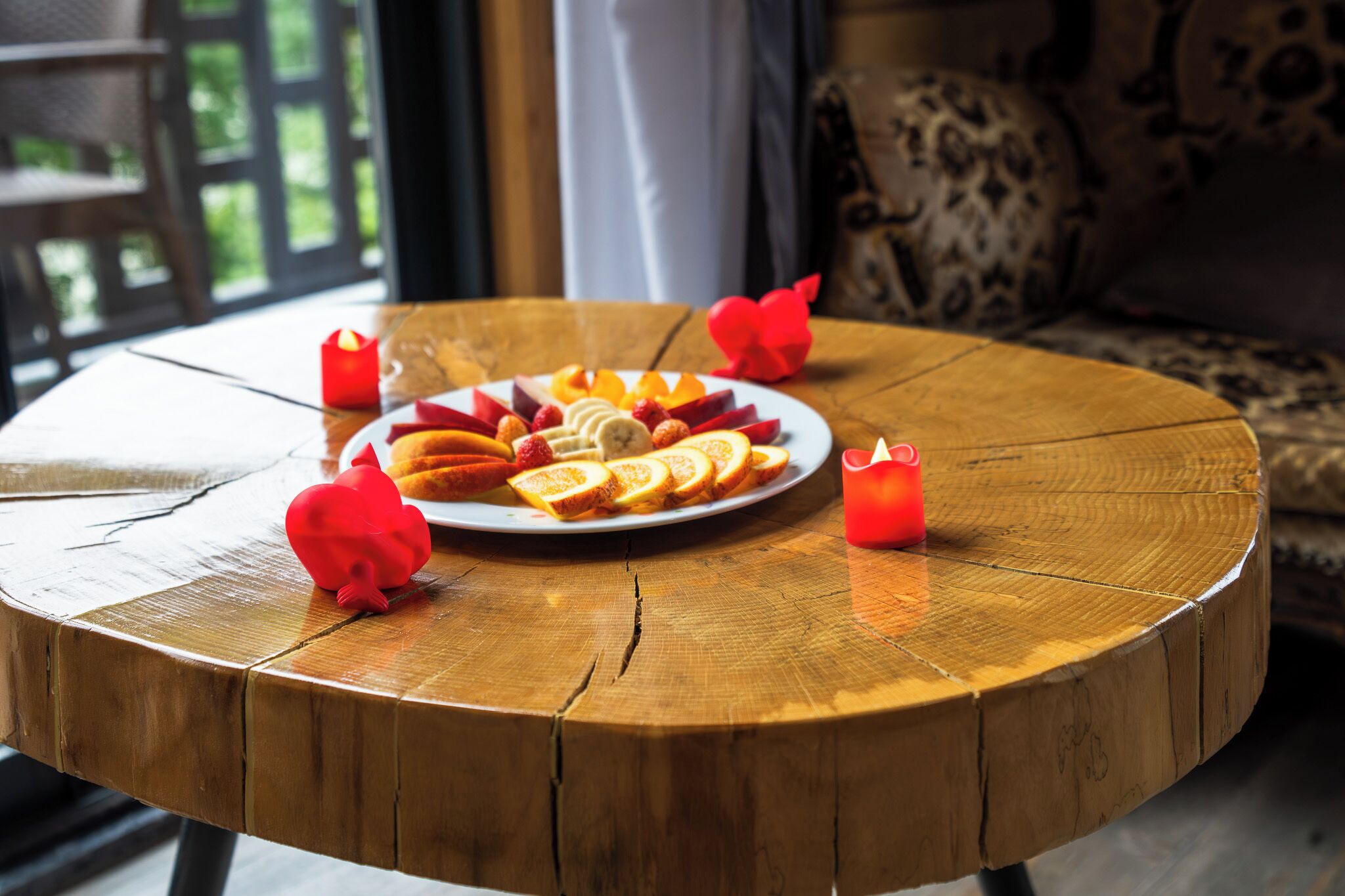 A round wooden table with a plate of fruit and candles.