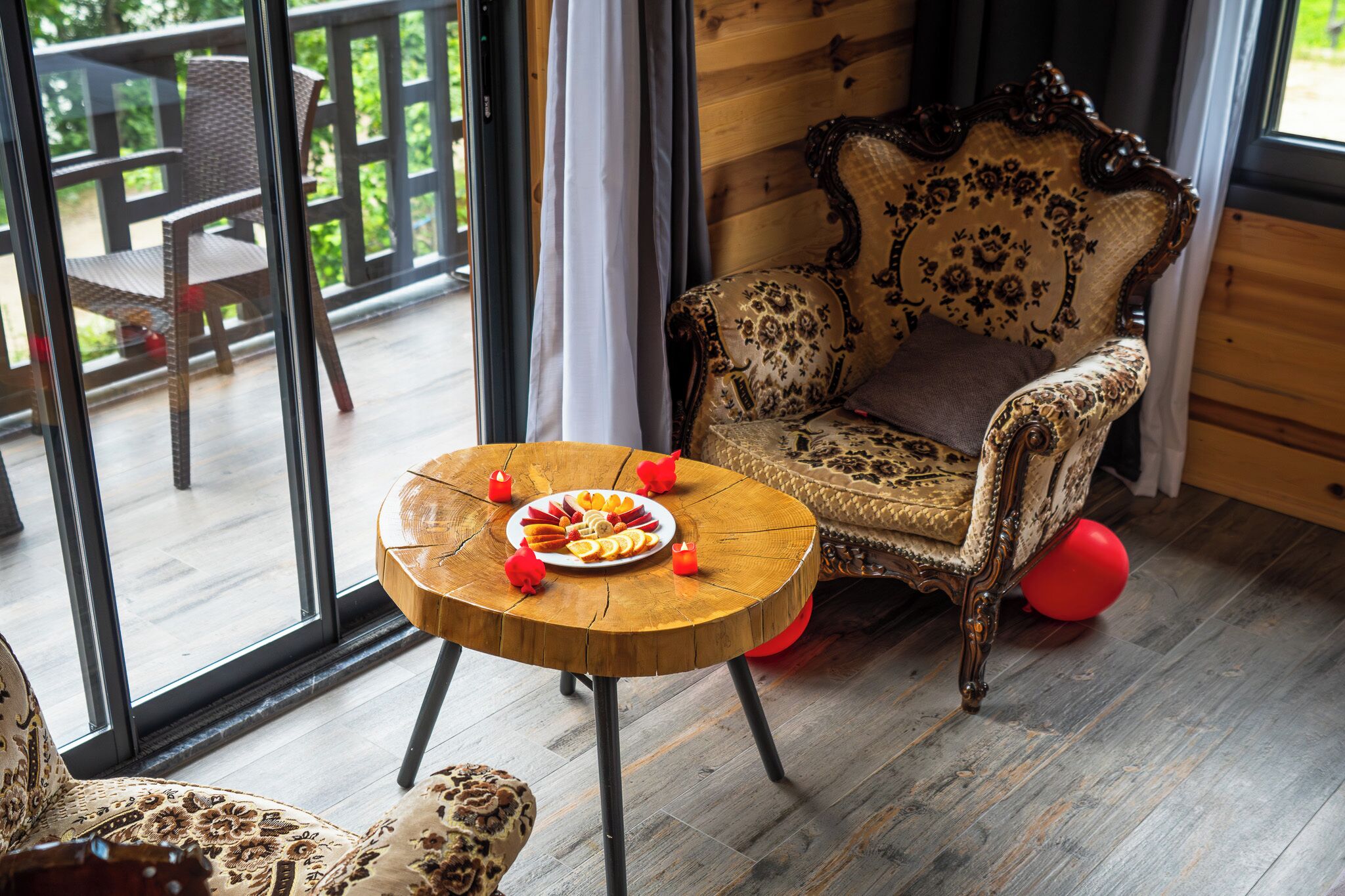 Une pièce dotée d’un plancher en bois, d’une table ronde en bois sur laquelle se trouve une assiette de fruits, d’un fauteuil à motifs et d’une vue dégagée grâce à de grandes fenêtres.