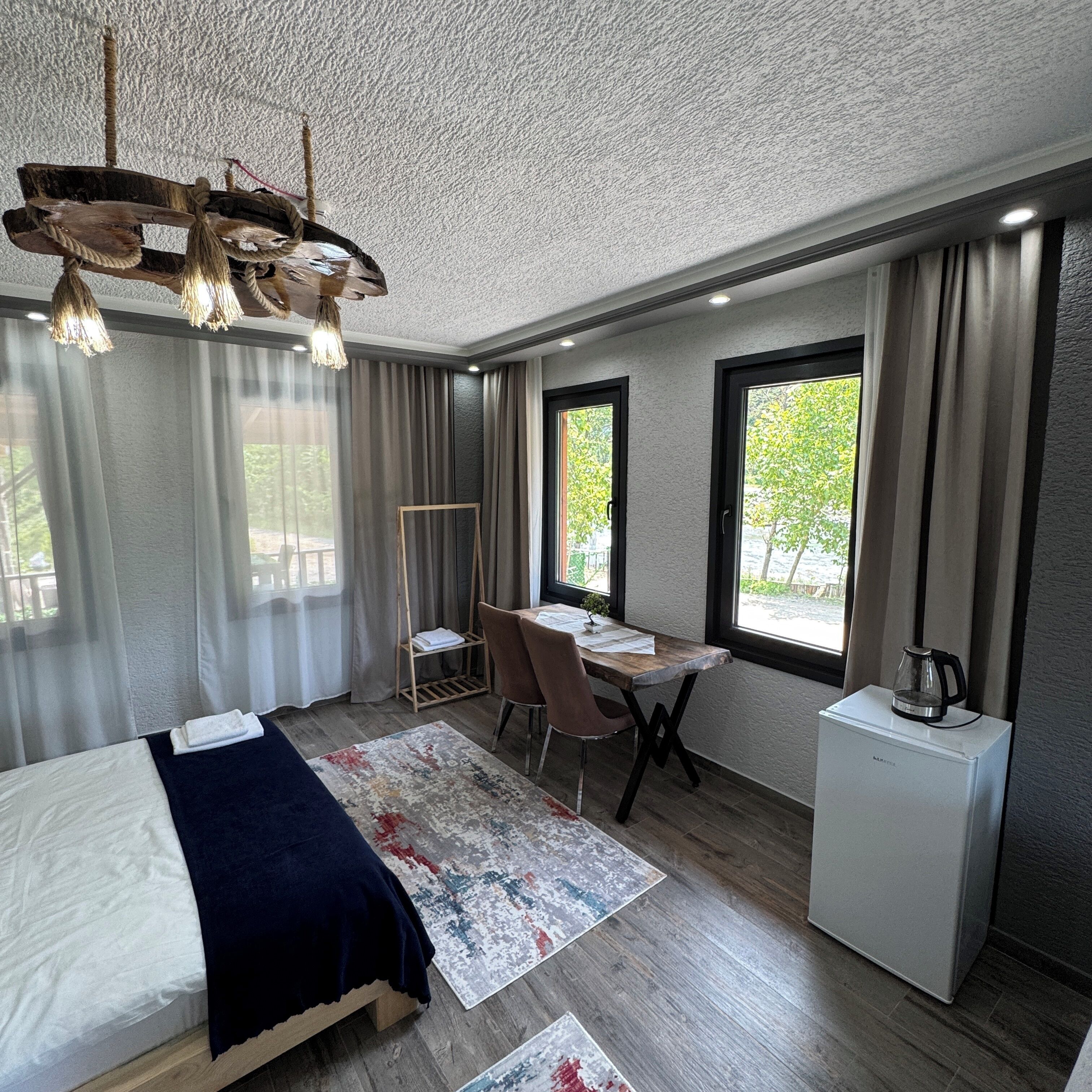 A modern hotel room with a bed, desk, chair, and a small kitchenette.