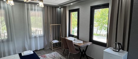 A modern hotel room with a bed, desk, chair, and a small kitchenette.