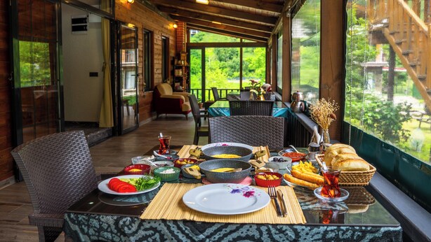 Un comedor con una mesa dispuesta para una comida, una silla de mimbre y vistas a la vegetación exterior.