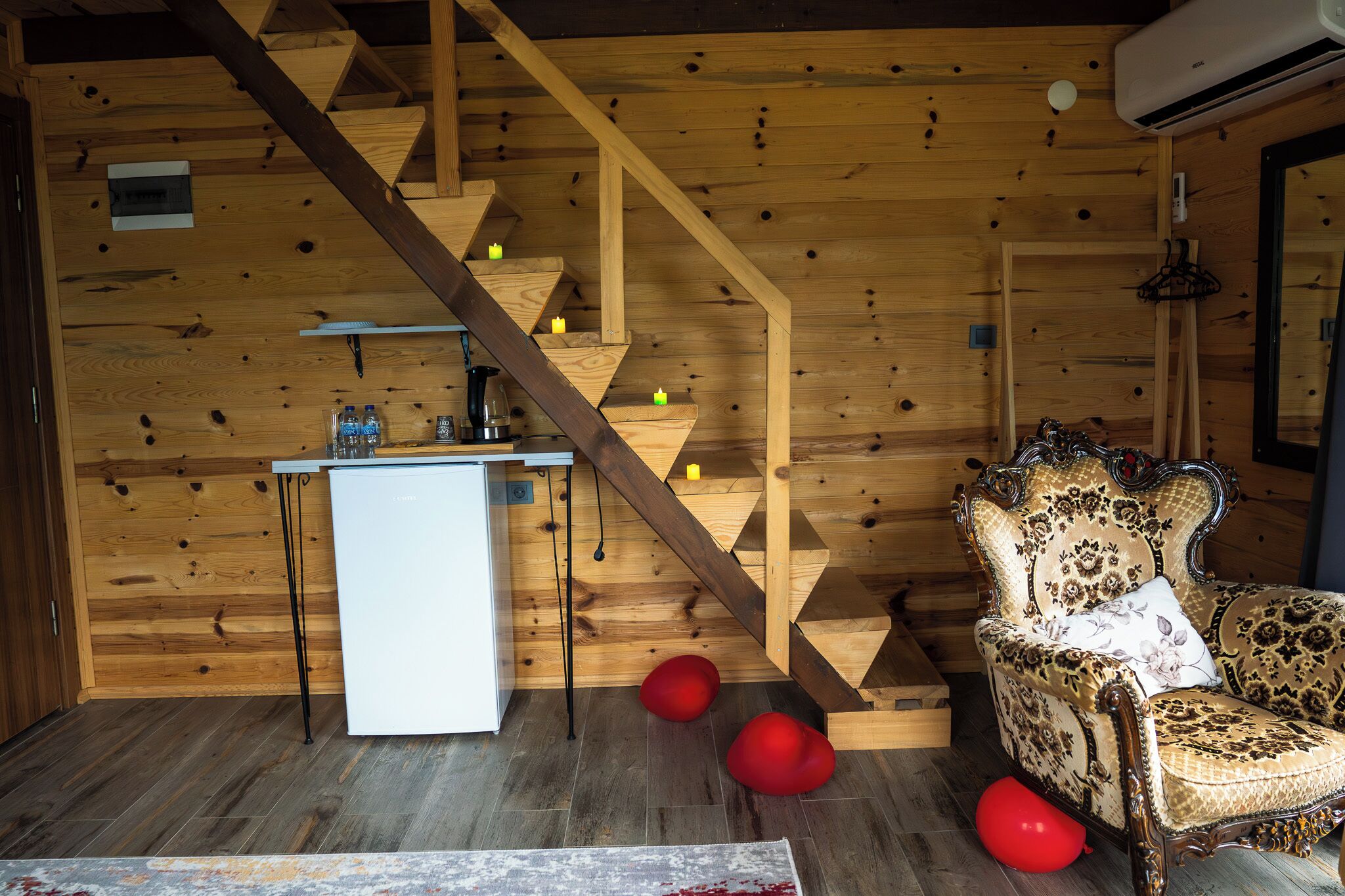 Een houten interieur met een trap, een wit bureau, een gestreept fauteuil en rode zakkenstoelen.