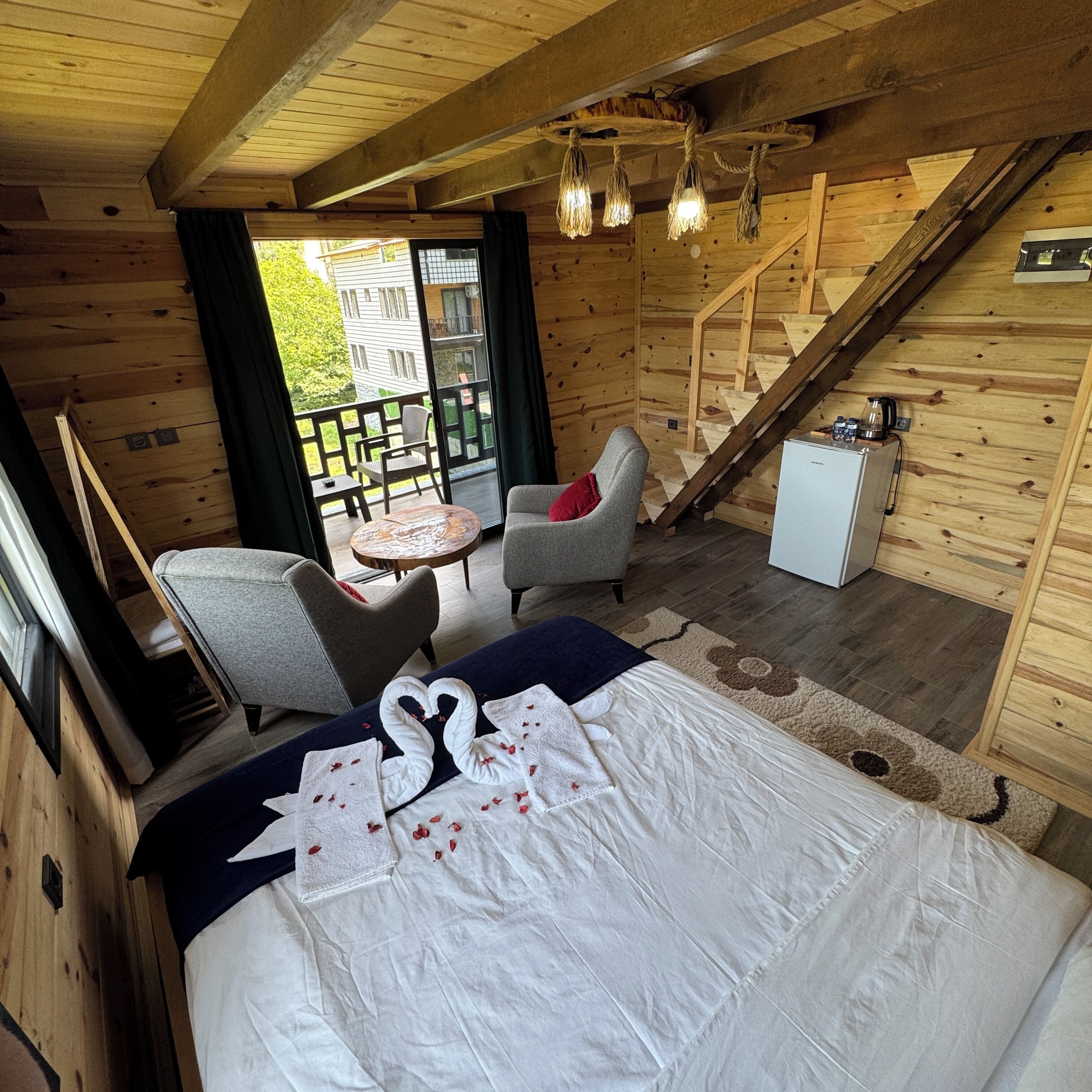 A cozy wooden cabin room with a bed, two chairs, a small table, and a staircase.