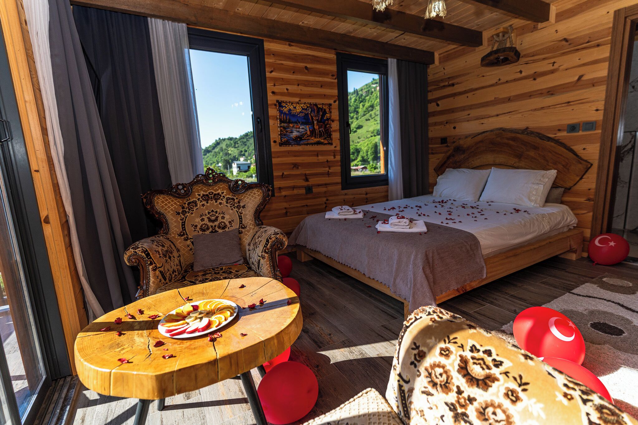 Una habitación de cabaña de madera con una cama, un sofá, una mesa con fruta y vistas al exterior.