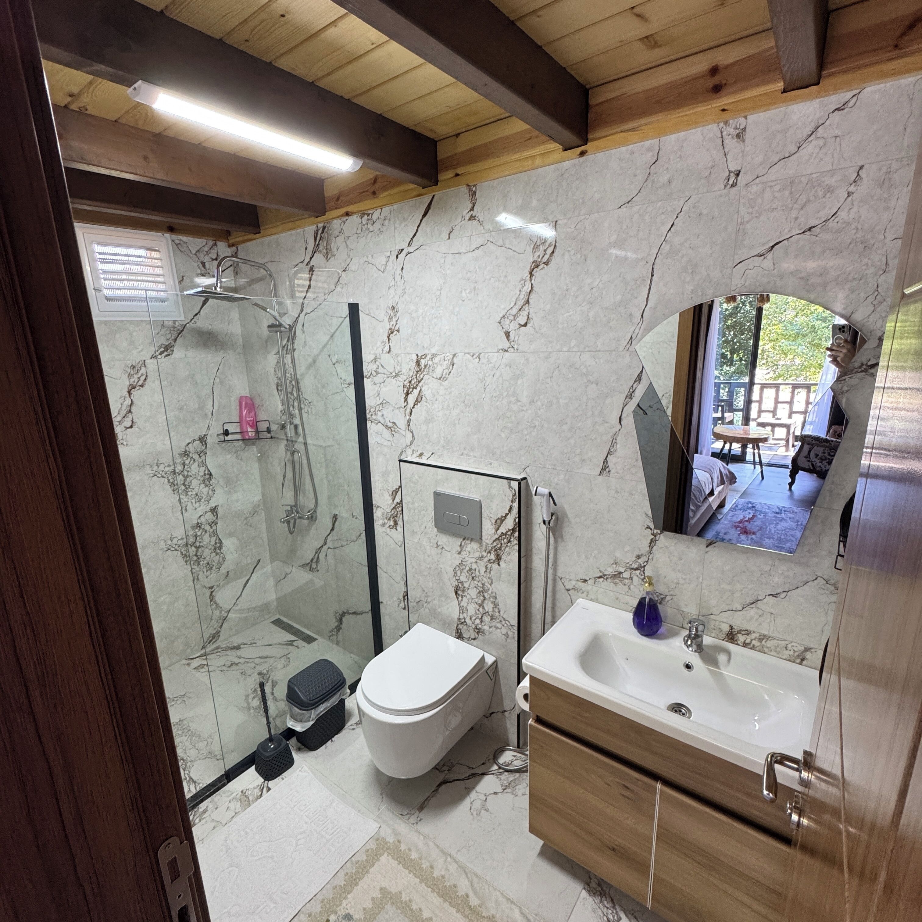 Ein modernes Badezimmer mit Duschkabine aus Glas, einer weißen Toilette und einem Holzausleger mit Waschbecken.