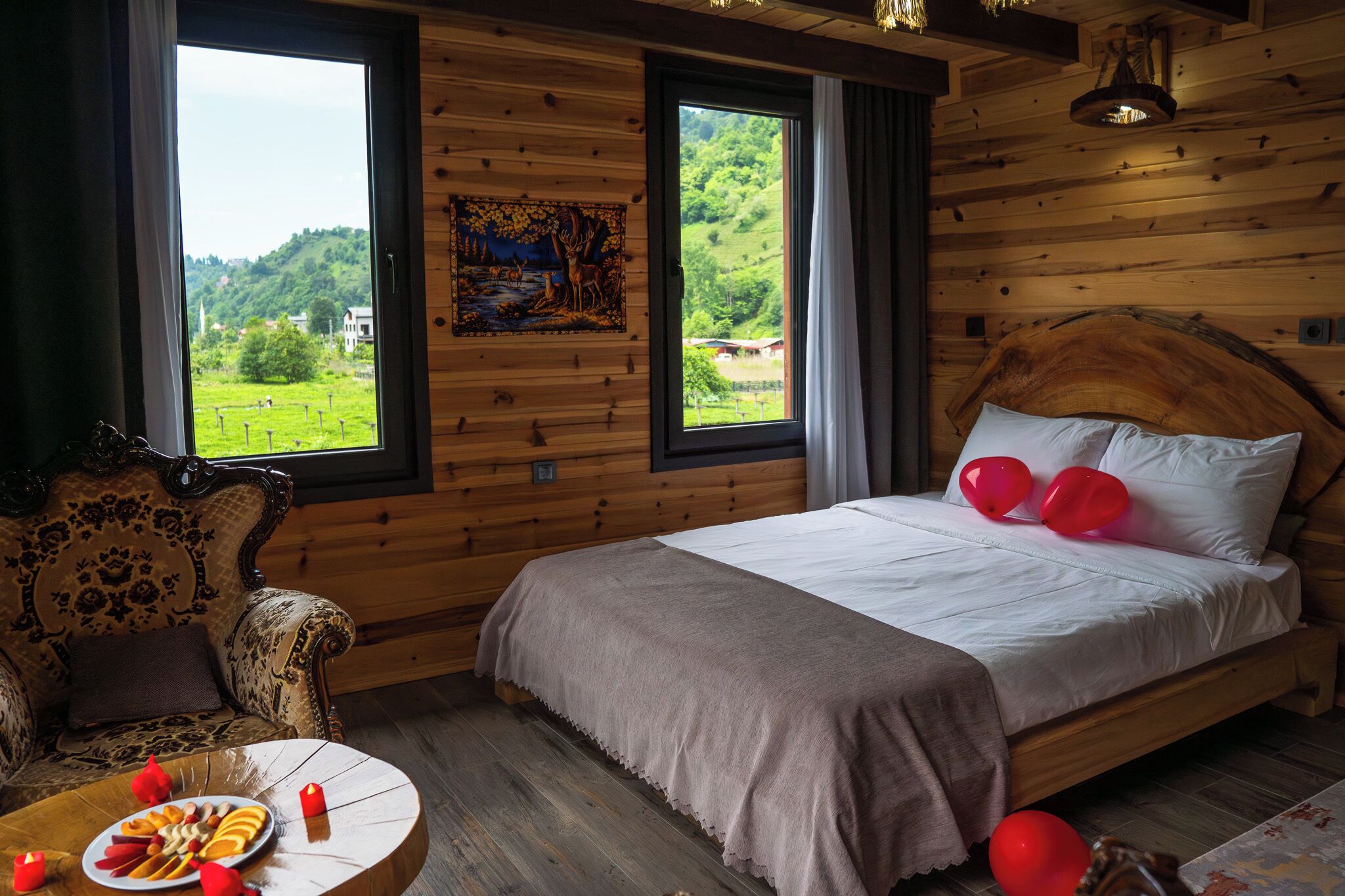 Una habitación de cabaña de madera con una cama, un sofá, una mesa con comida y dos ventanas con vistas.