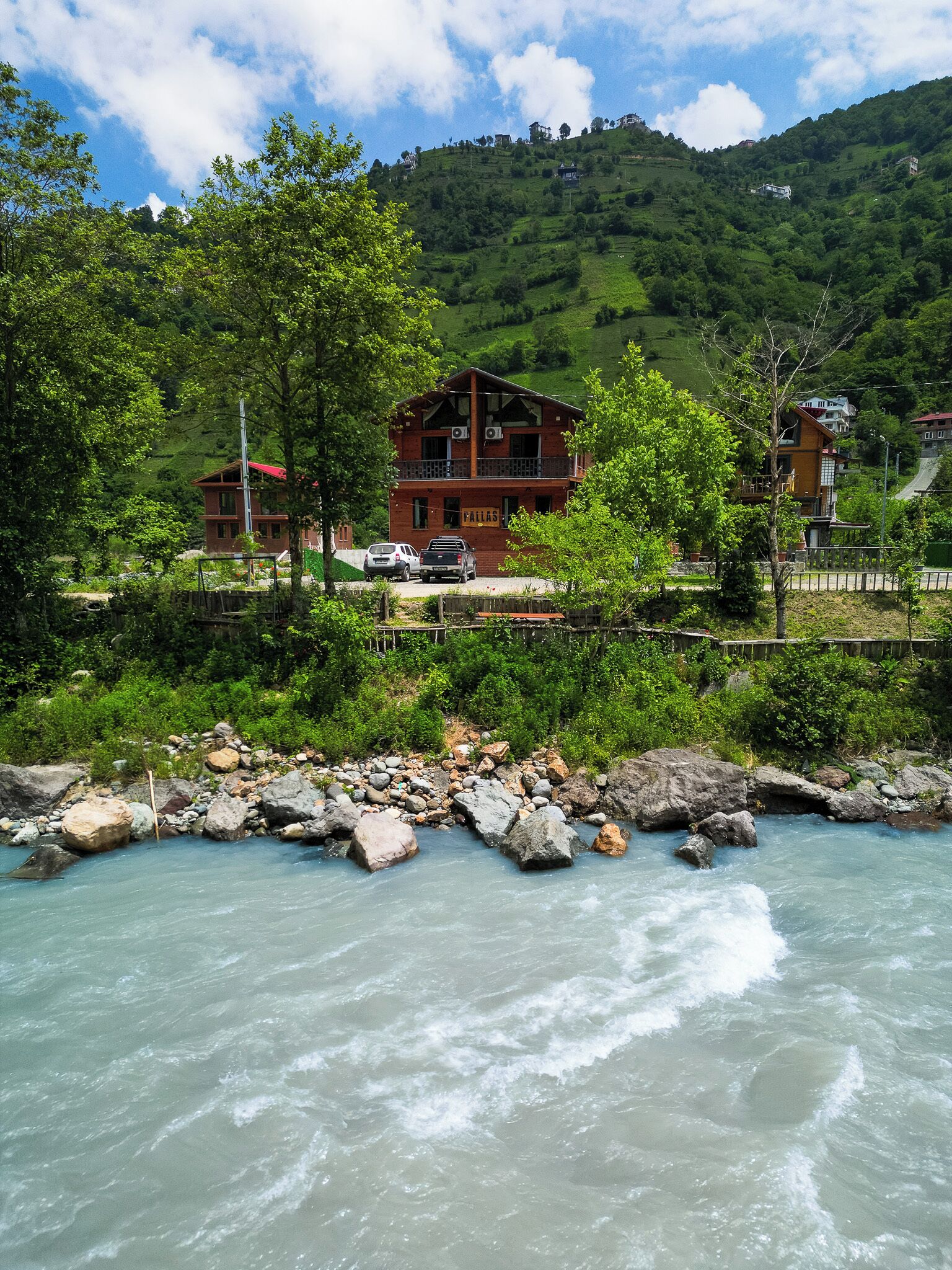 A riverside view with a wooden building, a bridge, and a mountainous backdrop.