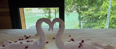 Una cama con una toalla dispuesta en forma de corazón y pétalos de rosa esparcidos.