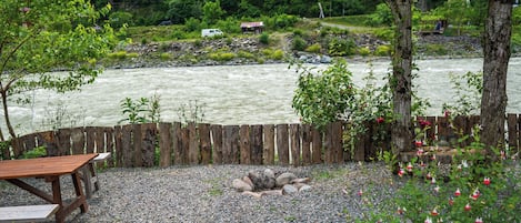 Un campamento a la orilla del río con vallas de madera, mesas de picnic y un pozo para fuego.
