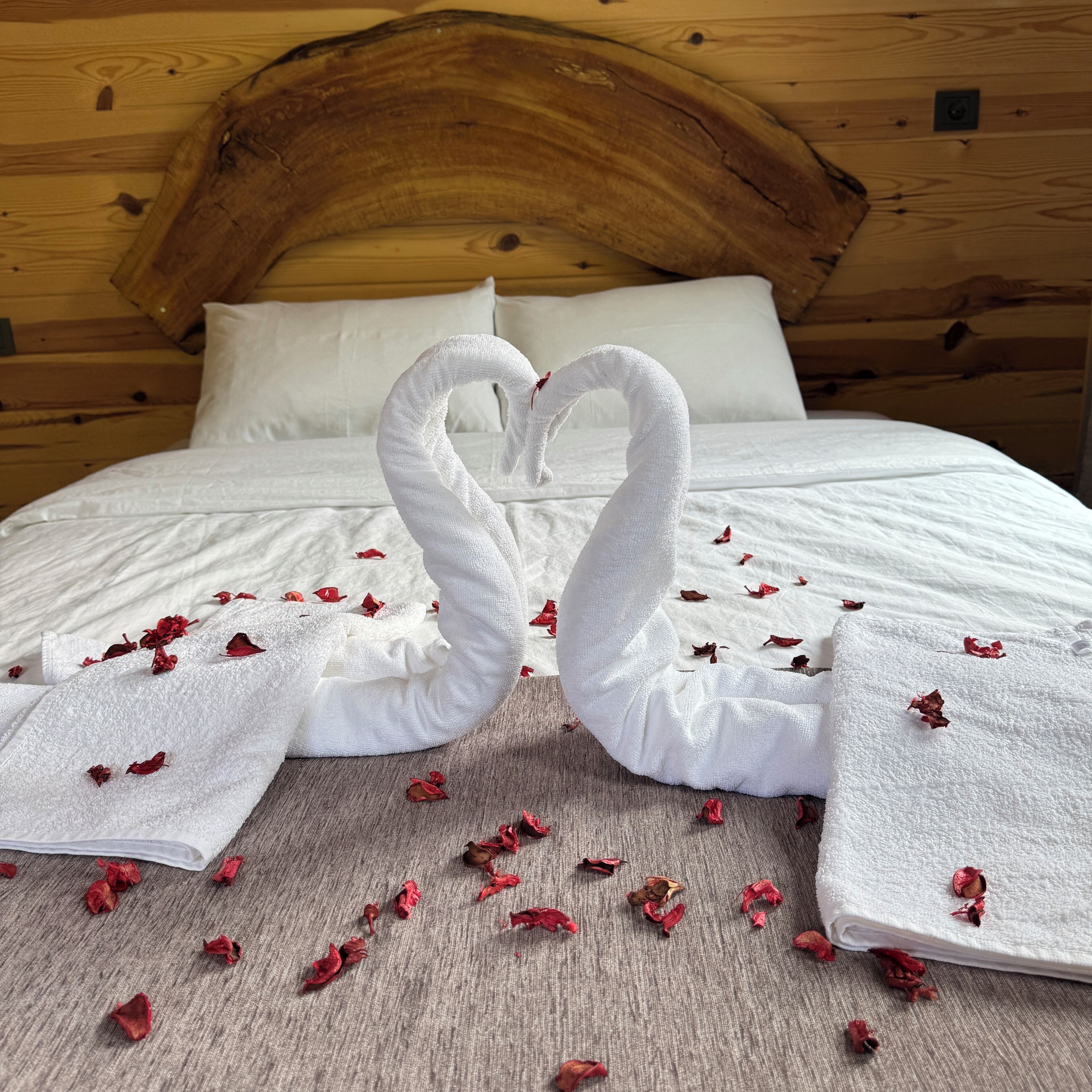 Un lit avec des draps blancs et deux serviettes disposées en forme de cœur.