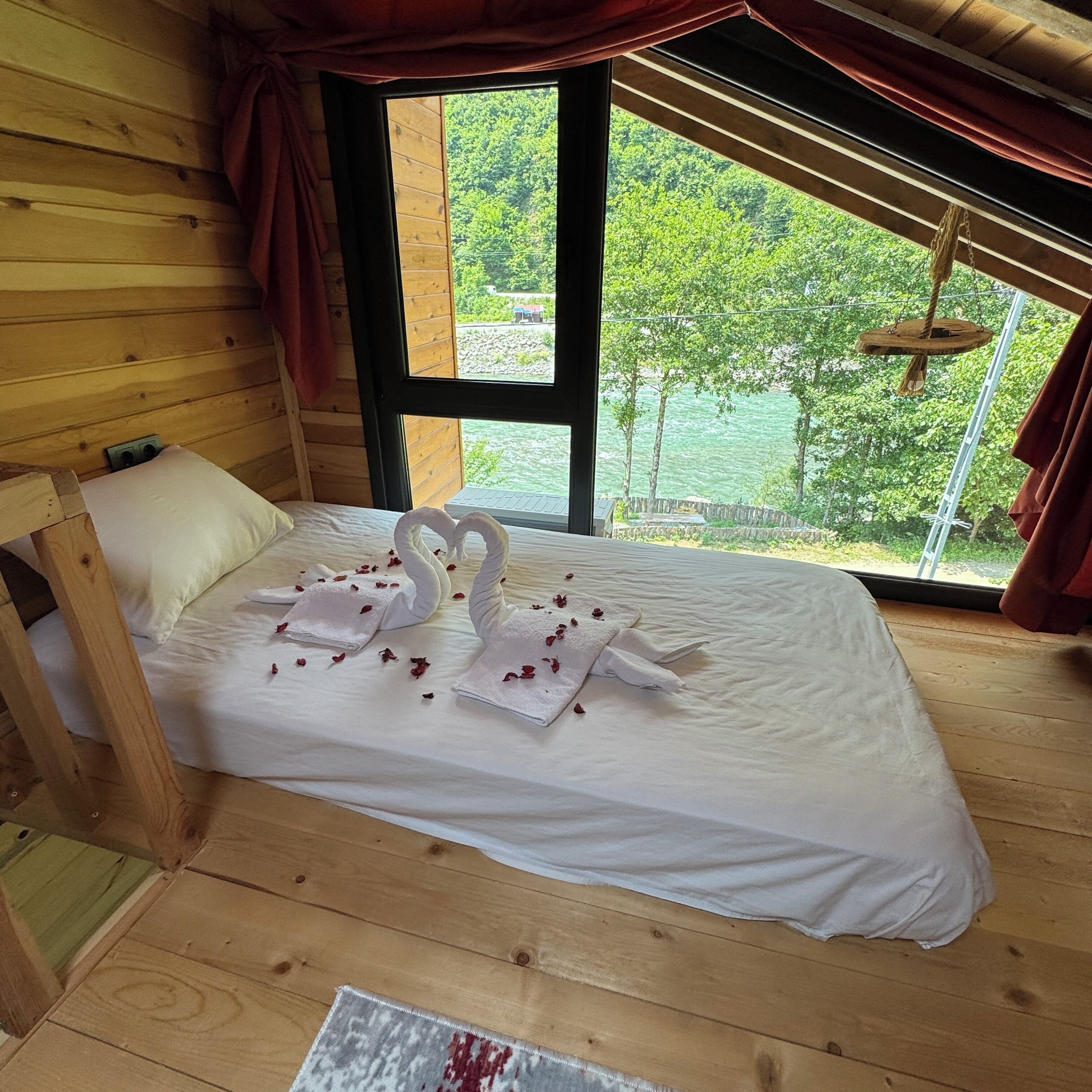 A wooden cabin bedroom with a bed, a window, and a view of greenery.