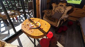 Een houten eettafel met een fruitschaal, een gestreept fauteuil en uitzicht op een houten terras door een glazen deur.