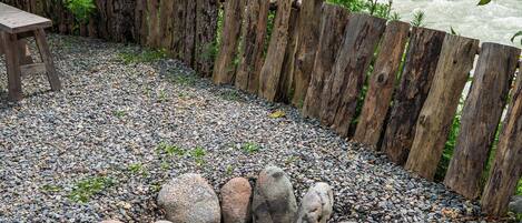 A gravel area with a fire pit, wooden fence, and a river view.
