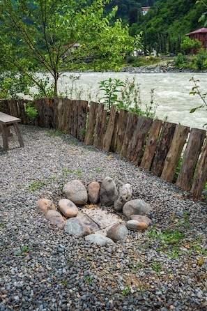 Zona de grava con un hogar, valla de madera y vista al río.