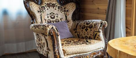 A vintage armchair with floral upholstery, a round wooden side table, and a wooden paneled wall.