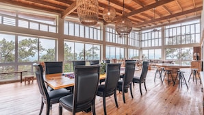 A spacious dining area with a wooden table and chairs, large windows, and hanging wicker chandeliers. - Mountain Views 11br 20 People Jarabacoa (Jarabacoa)