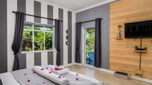 Un dormitorio moderno con una cama grande, un televisor instalado en una pared de madera y una ventana con cortinas.