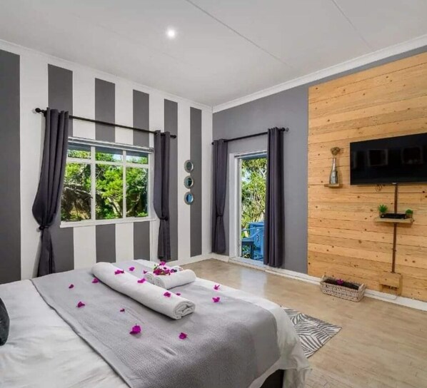 Een moderne slaapkamer met een groot bed, een aan een houten wand bevestigde televisie en een raam met gordijnen.