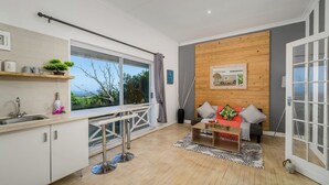Una cocina moderna con un ventanal grande, un comedor con mesa de madera y una sala de estar con sofá y vistas al exterior.