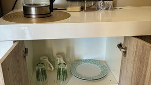 Et køkken med elkedel, beholdere og et skab med service og glas.