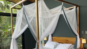 Un letto a baldacchino con tende, biancheria bianca, due cuscini con la scritta 'CHEER' e un tappeto verde sul pavimento.