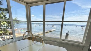 Een zonnige kamer met een grote tafel en stoelen, en grote ramen met uitzicht op zee en boten.