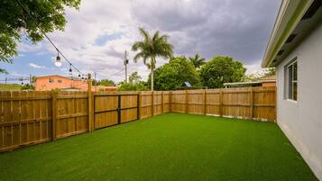 A fenced backyard with artificial grass, a wooden fence, and a palm tree.