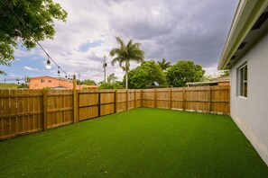 Un patio trasero cercado con césped artificial, una valla de madera y una palmera.