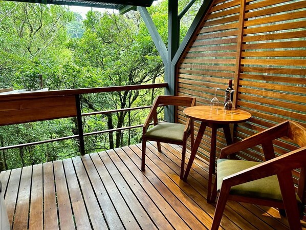 A wooden deck with a table and chairs, overlooking a forested area.