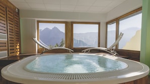 A hot tub with wooden walls and large windows offering mountain views.