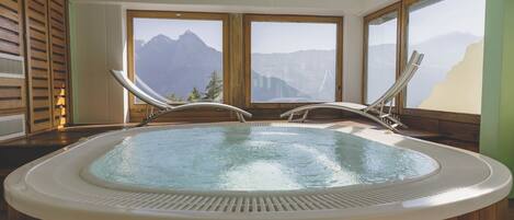 A hot tub with wooden walls and large windows offering mountain views.
