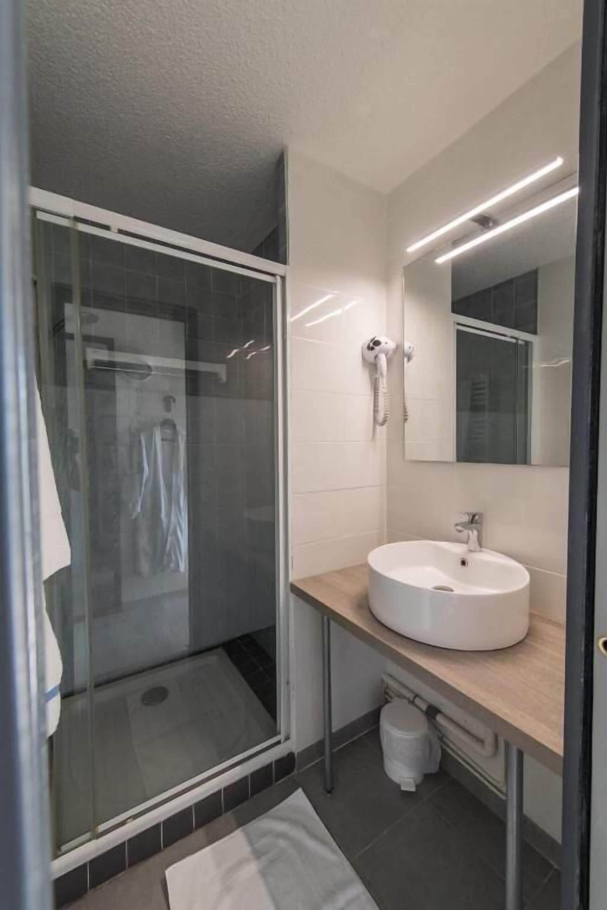 A modern bathroom with a glass-enclosed shower, a round sink, and a mirror above it.