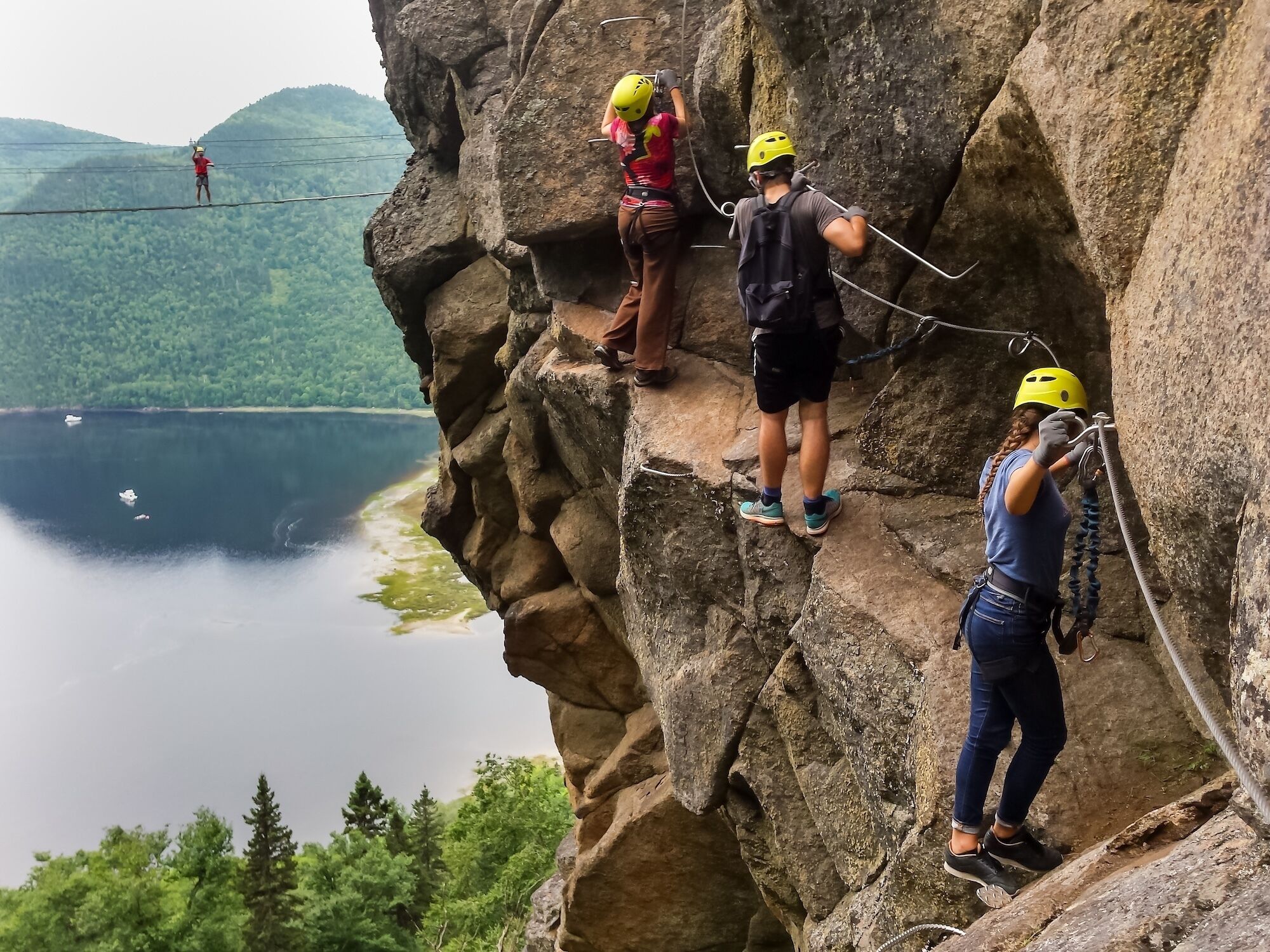 Un grupo de personas escalando en un risco, con un lago y un bosque al fondo.