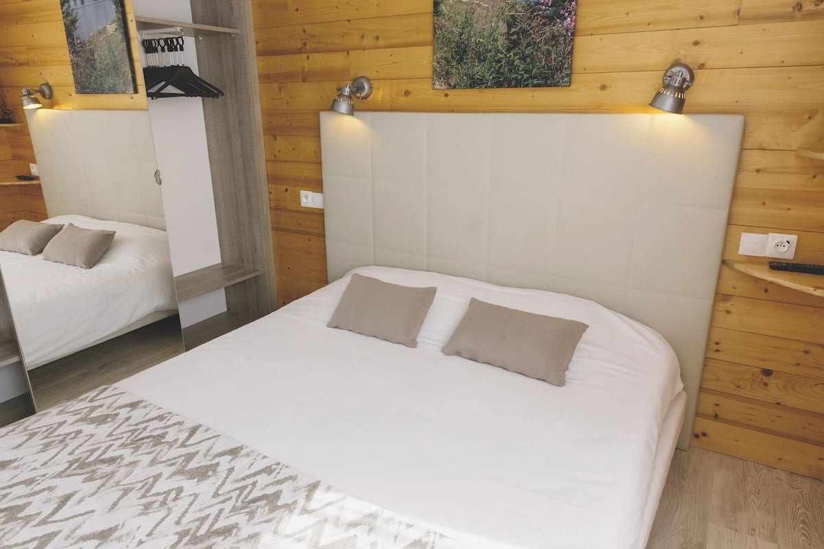 Ein Hotelzimmer mit einem großen Bett, einem kleineren Bett, Holzvertäfelung, einer Wandleuchte und einem Gemälde.