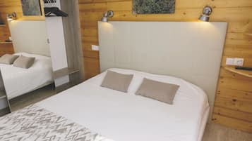 A hotel room with a large bed, a smaller bed, wooden paneling, a wall-mounted light, and a painting.