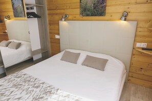 A hotel room with a large bed, a smaller bed, wooden paneling, a wall-mounted light, and a painting. - Club Vacances Bleues Arc-en-ciel - Ski Pass Inclus (Montricher-Albanne)