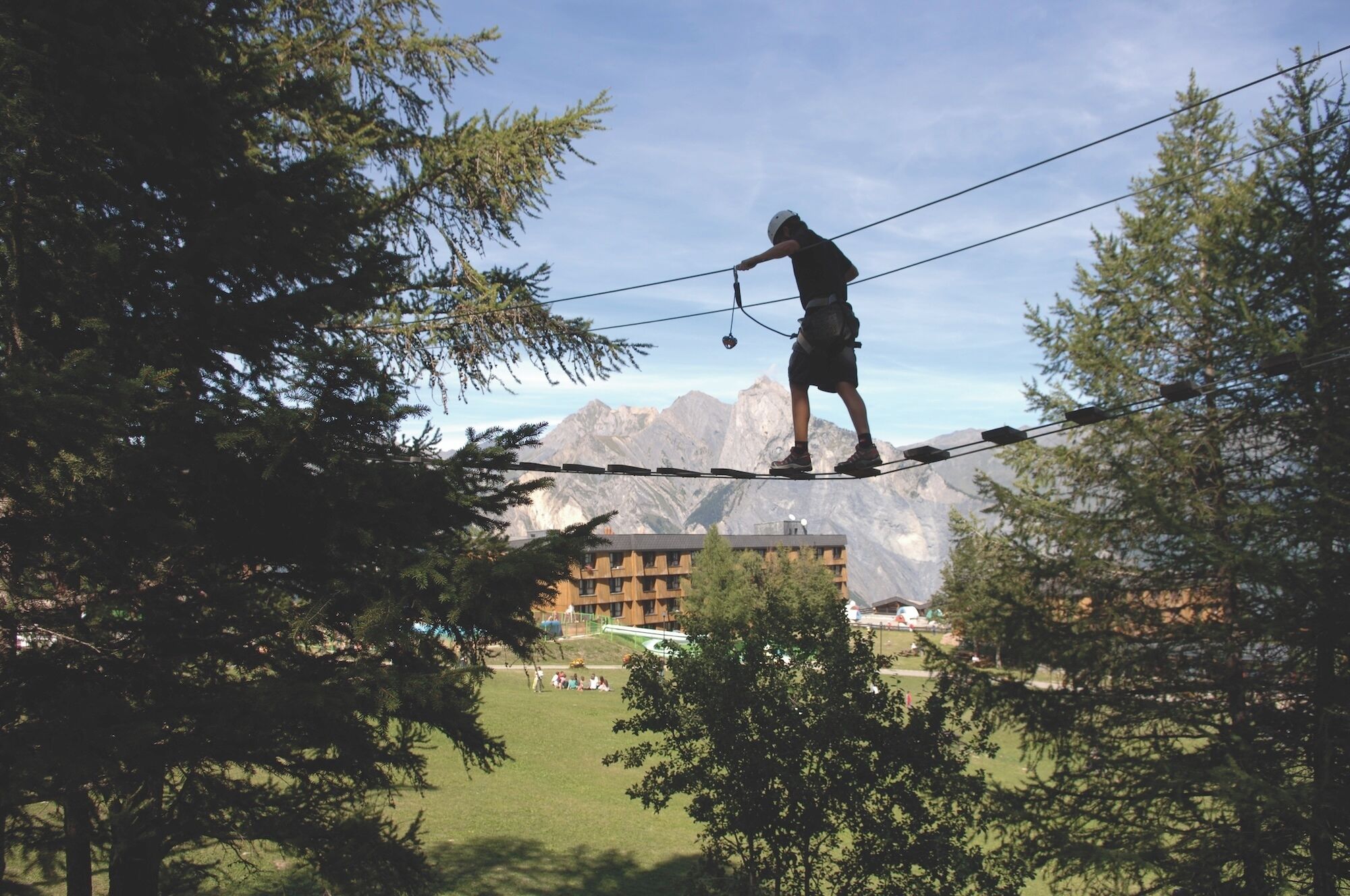 A person walking on a rope bridge with mountains in the background.