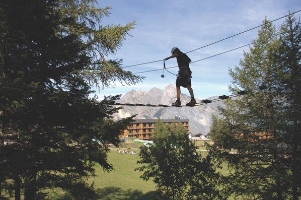 A person walking on a rope bridge with mountains in the background. - Club Vacances Bleues Arc-en-ciel - Ski Pass Inclus (Montricher-Albanne)