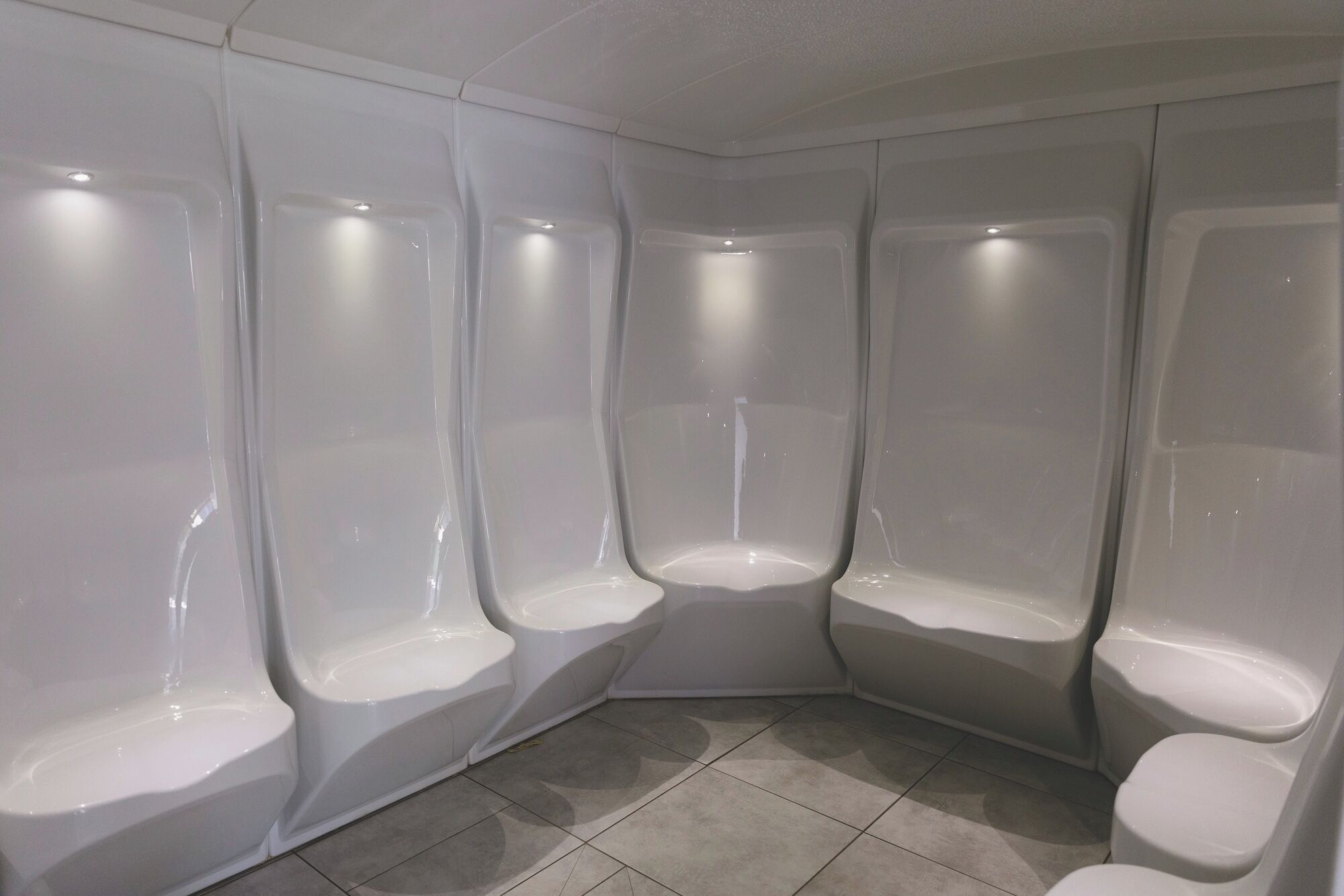 Un coin d’une salle de bain avec quatre urinoirs blancs et un sol carrelé.