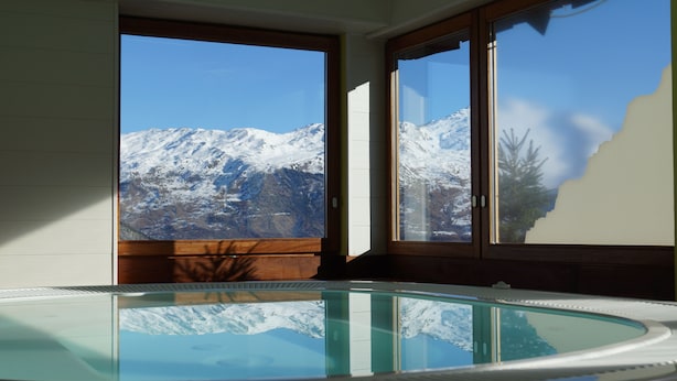 A room with a glass-enclosed hot tub and a view of snow-capped mountains.