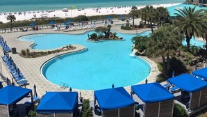 A resort with a large central pool, a beach, and a hotel building.