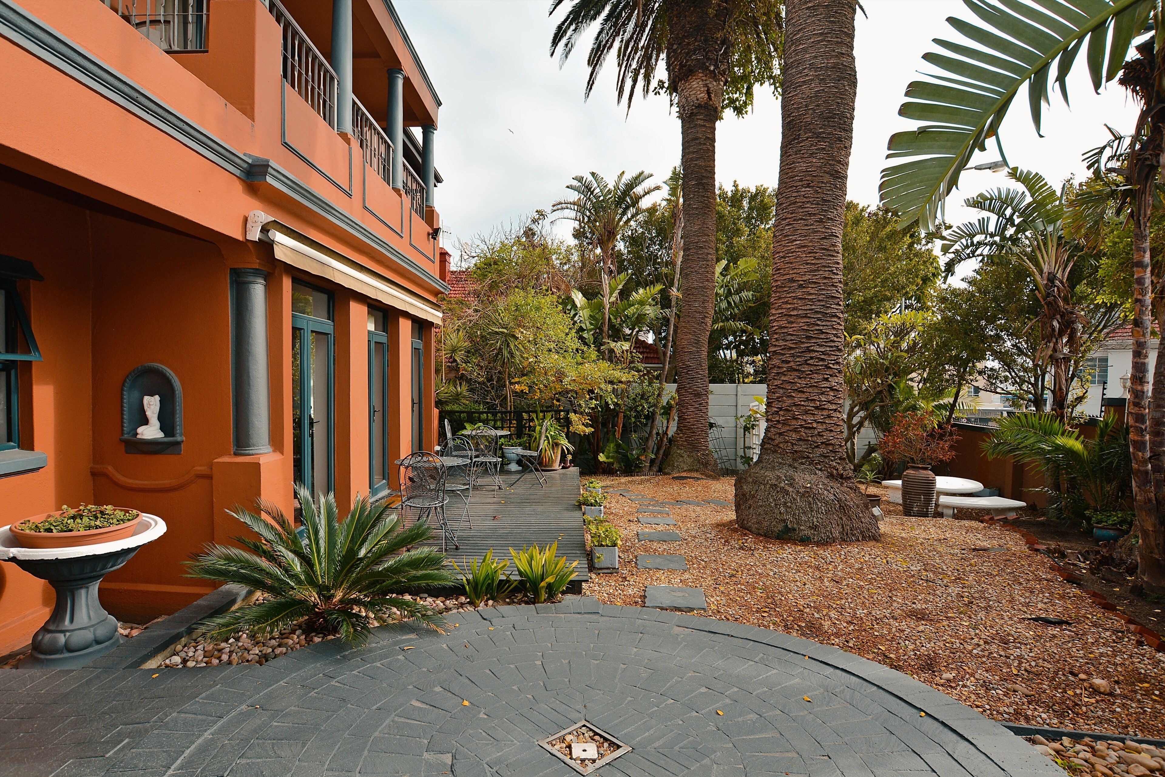 A courtyard with a paved walkway, palm trees, and a building with orange walls and green windows.