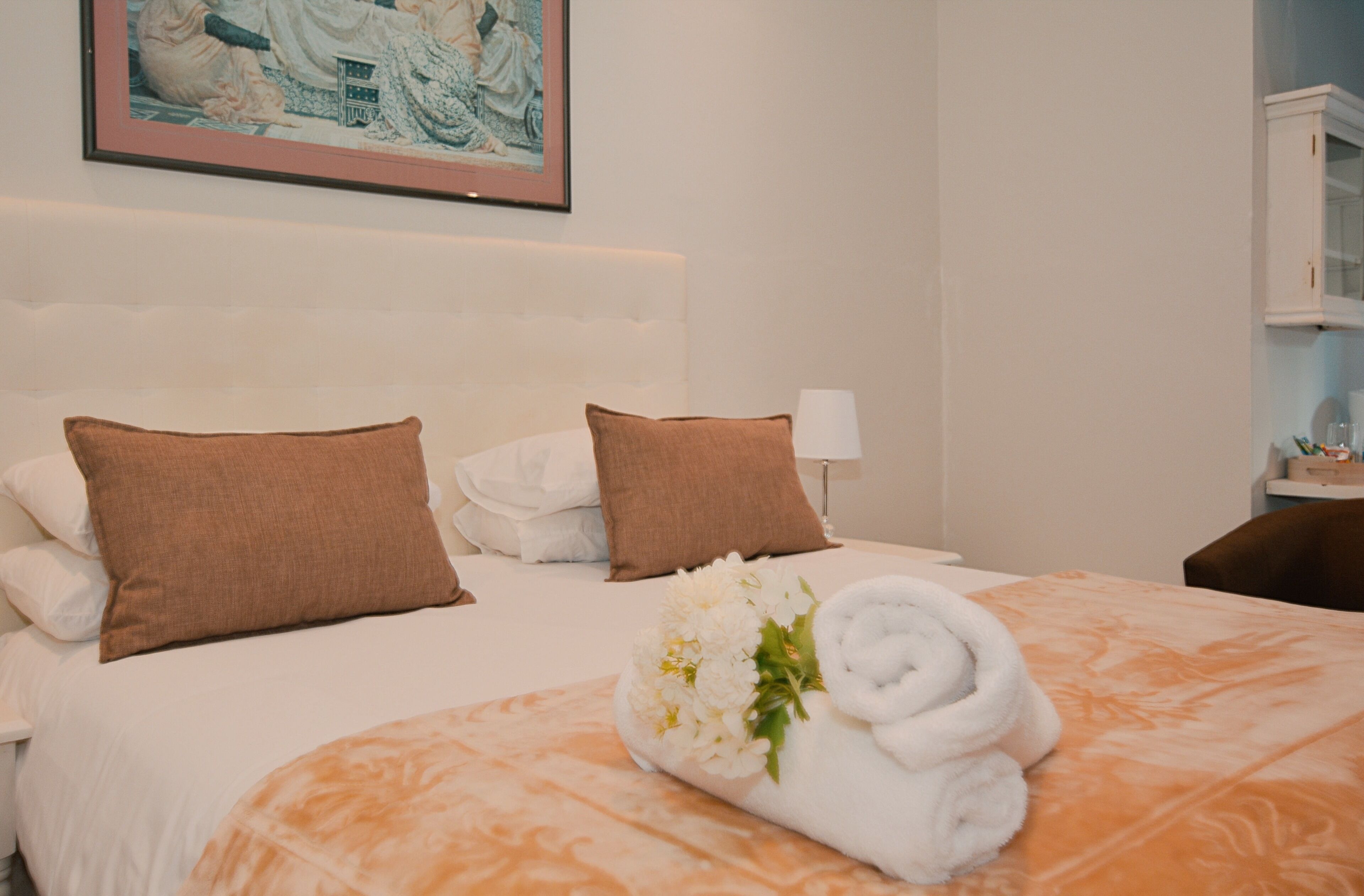 A hotel room with a bed, pillows, a rolled towel, and a framed picture on the wall.