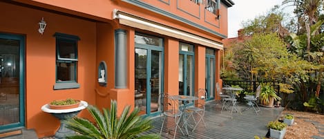 A two-story building with a balcony, outdoor seating, and potted plants.