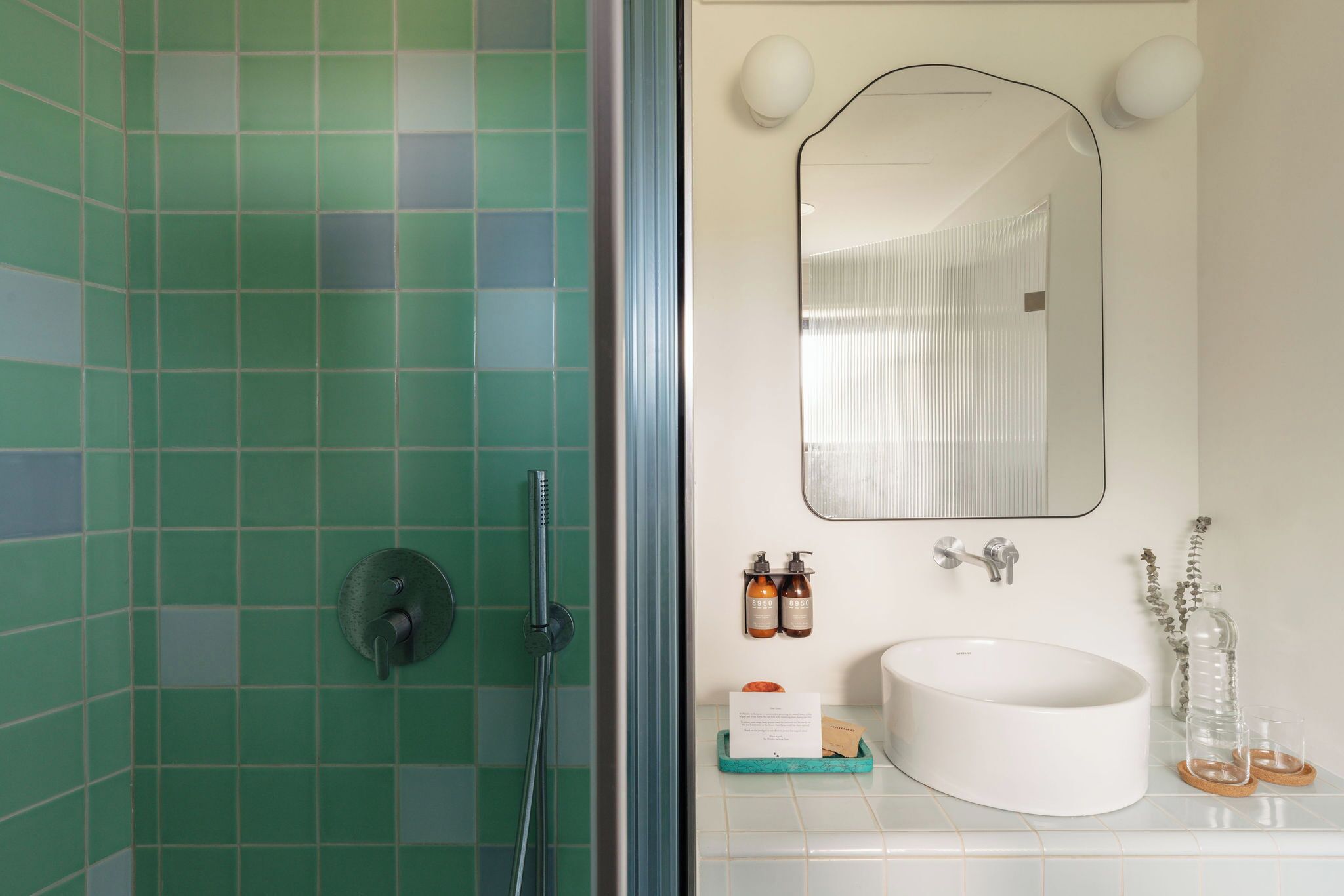 A bathroom with green tiled walls, a white sink, and a mirror above it.