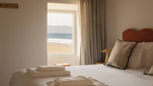 A hotel room with a bed, a window with a view of the beach, and a lamp on a bedside table. - Moinho da Areia (Ribeira Grande)