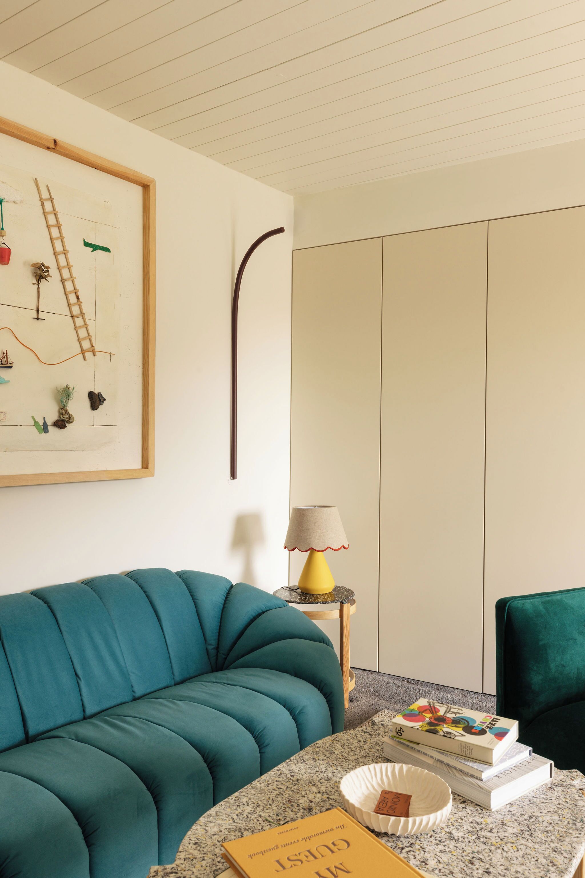 Un canapé de couleur turquoise, une petite table avec une lampe et un tableau abstrait encadré accroché au mur.